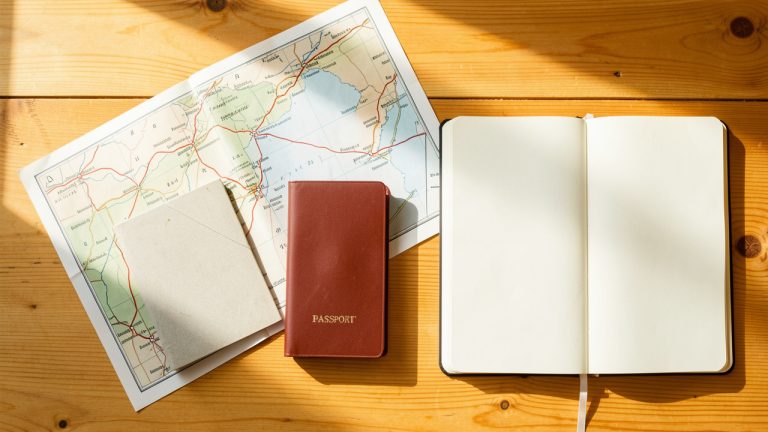 Nature morte lumineuse montrant une carte vierge du Maroc, un passeport fermé, un téléphone à écran vierge et un carnet ouvert sur une table en bois.